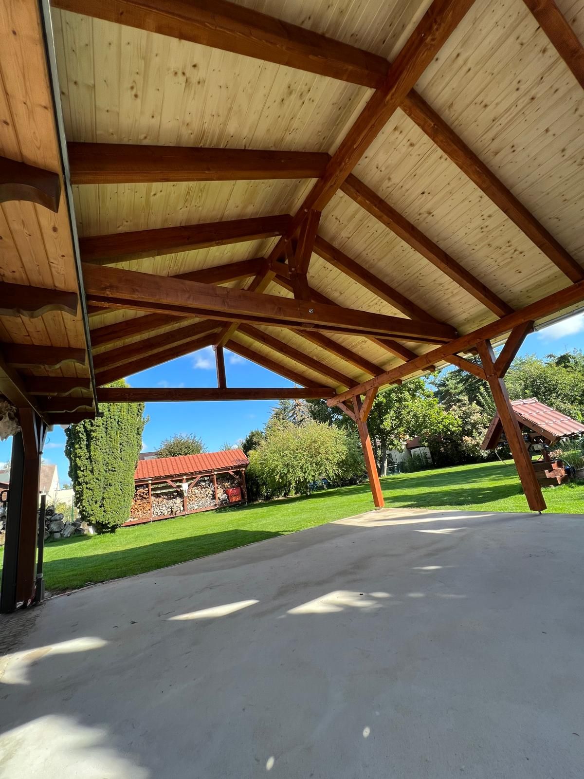Untersicht eines Holzcarports mit Satteldach, sichtbaren Sparren und heller Holzschalung, dahinter ein Garten