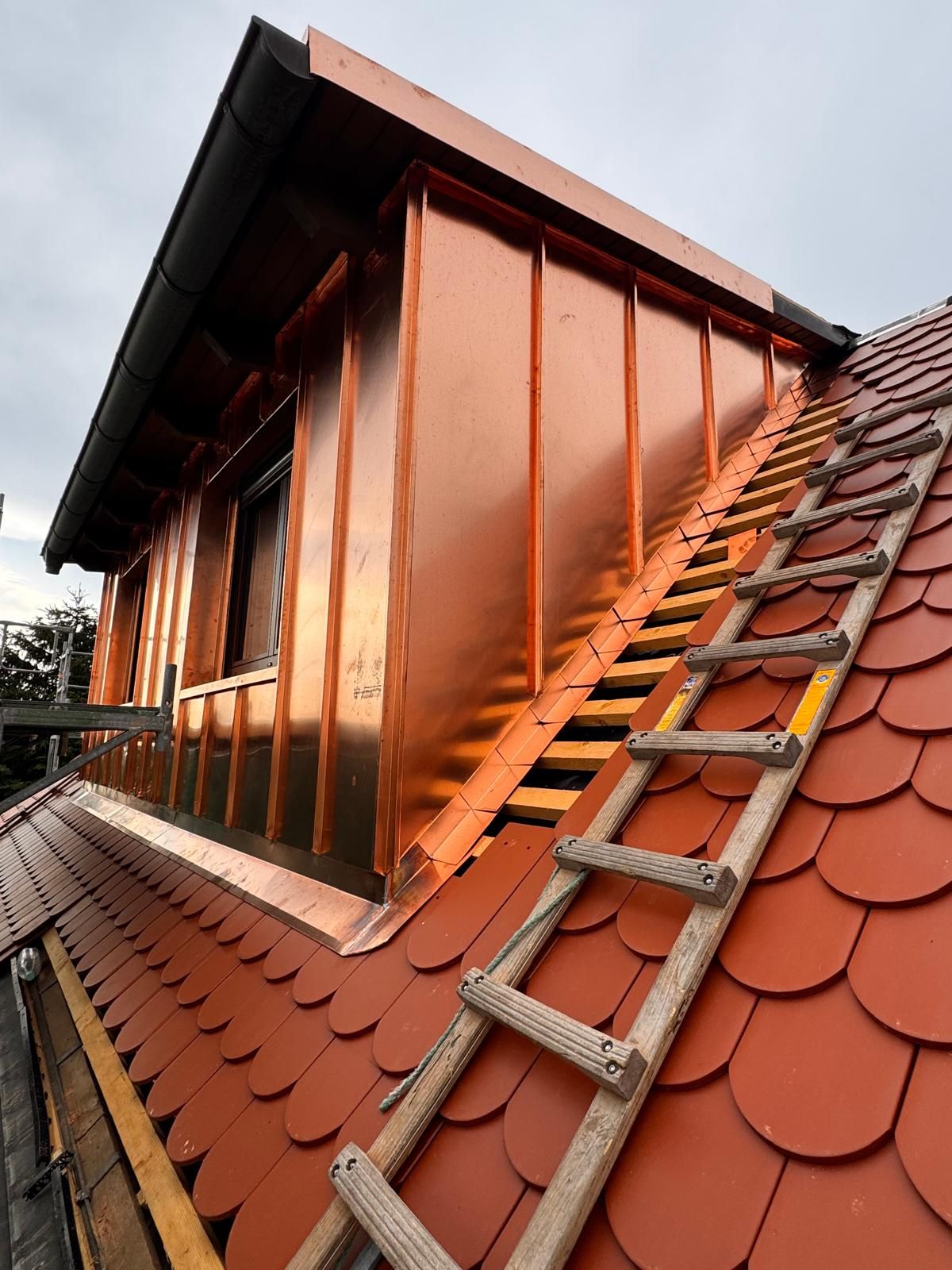 Mit Kupfer im Stehfalz bekleidete Dachgaube auf einem Dach mit roten Biberschwanzziegeln, davor eine Dachleiter