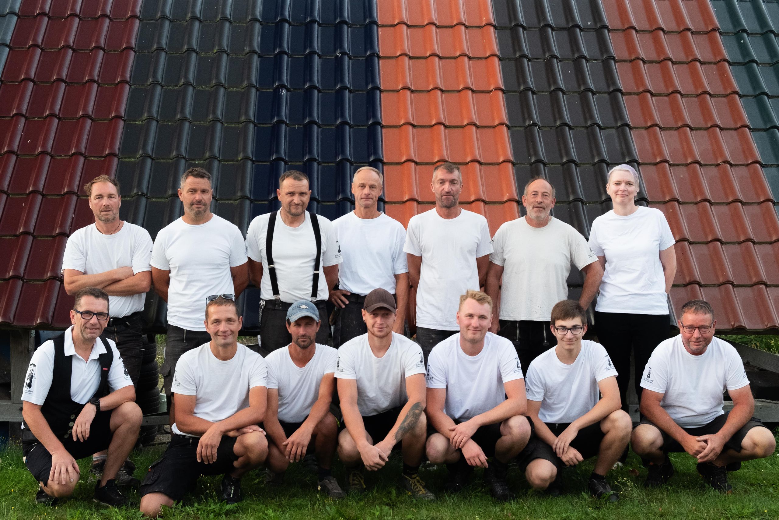 Das Team von Gebr. Rogat vor einer Musterdachfläche mit Dachziegeln in verschiedenen Farben