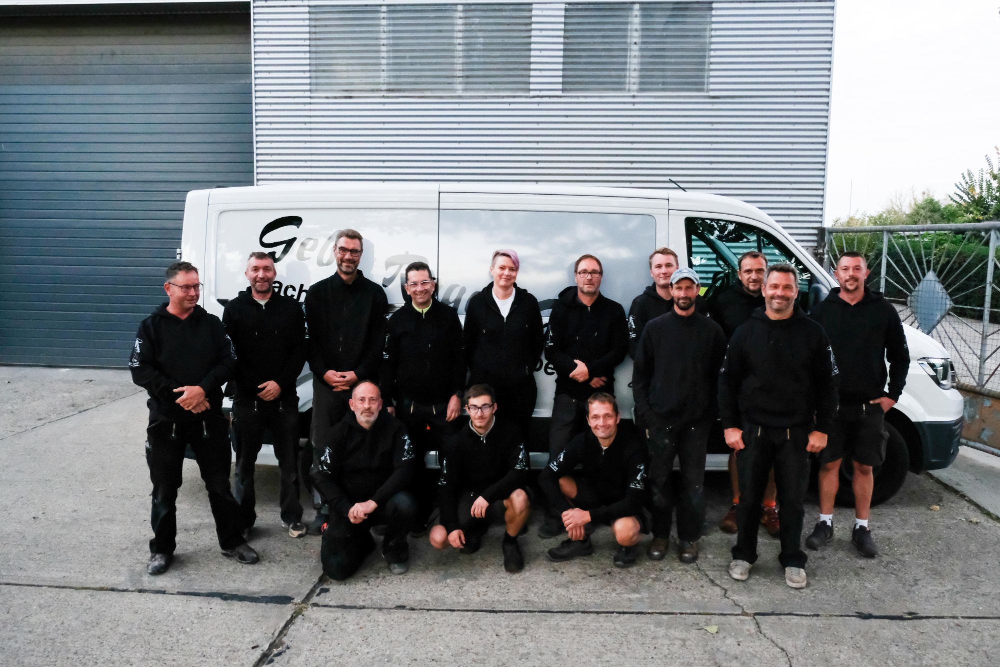 Das Team von Gebr. Rogat in schwarzer Arbeitskleidung vor dem Firmenwagen an der Halle